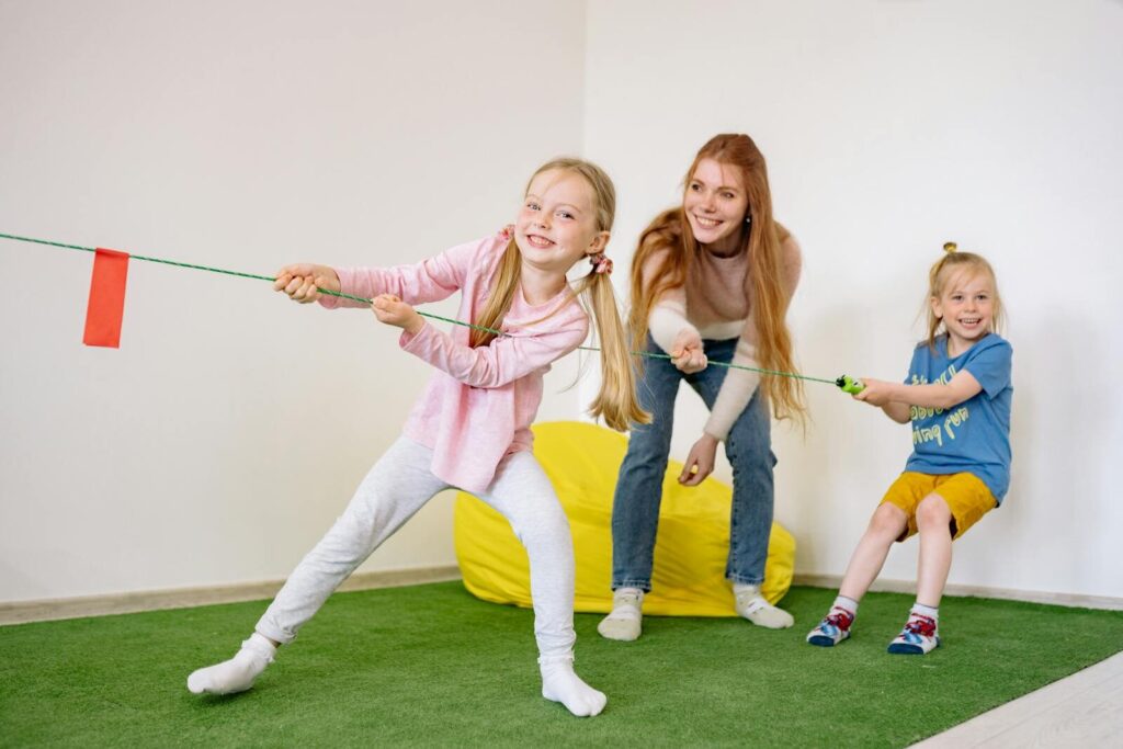 Kids and teacher enjoying a fun tug-of-war game in an indoor playroom setting.